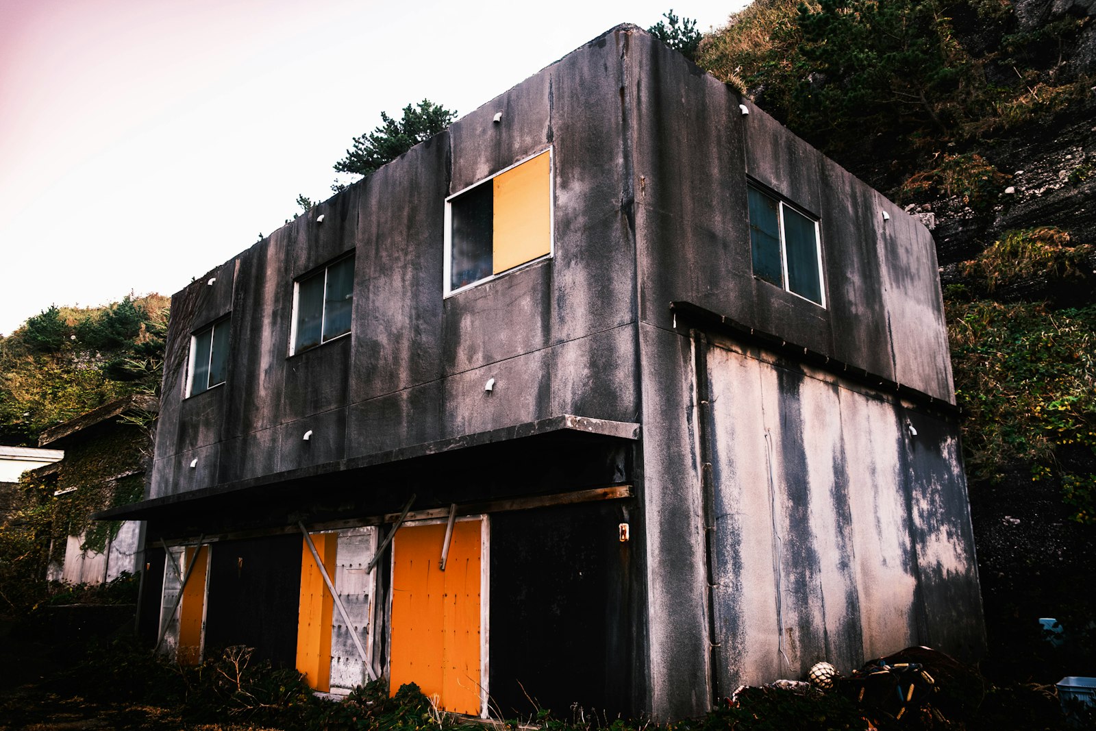 地方の傾斜地に建つ老朽化した2階建てアパート。窓が板でふさがれ長期間空室になっている外観
