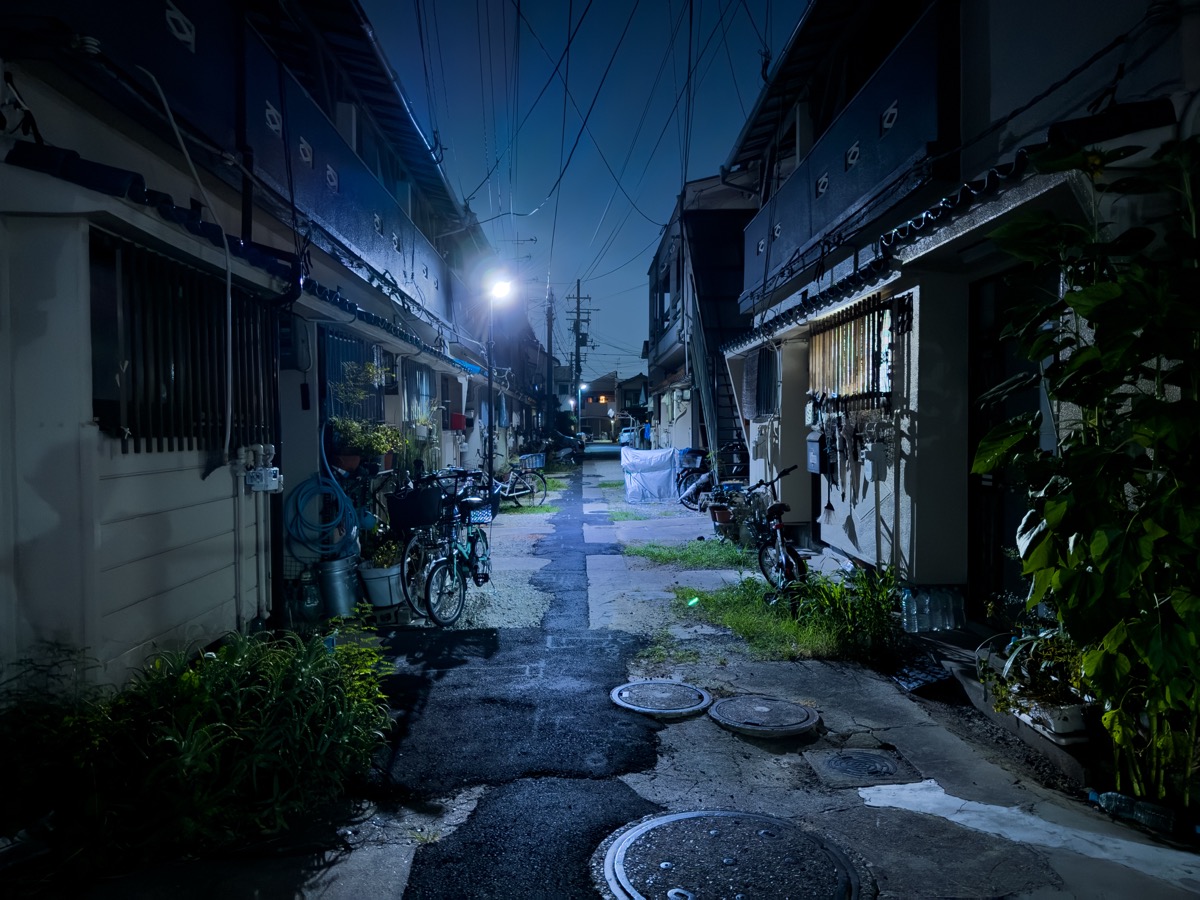 大阪市内の狭い路地。両側に木造2階建ての長屋が連なり、道幅は車が通れないほど狭い