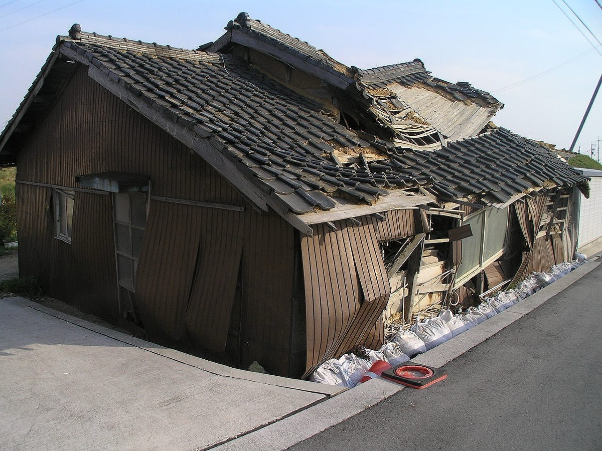 外壁と屋根が崩れ、土のうで支えられた老朽木造住宅　道路に面しており保安上危険な状態の特定空家等の例