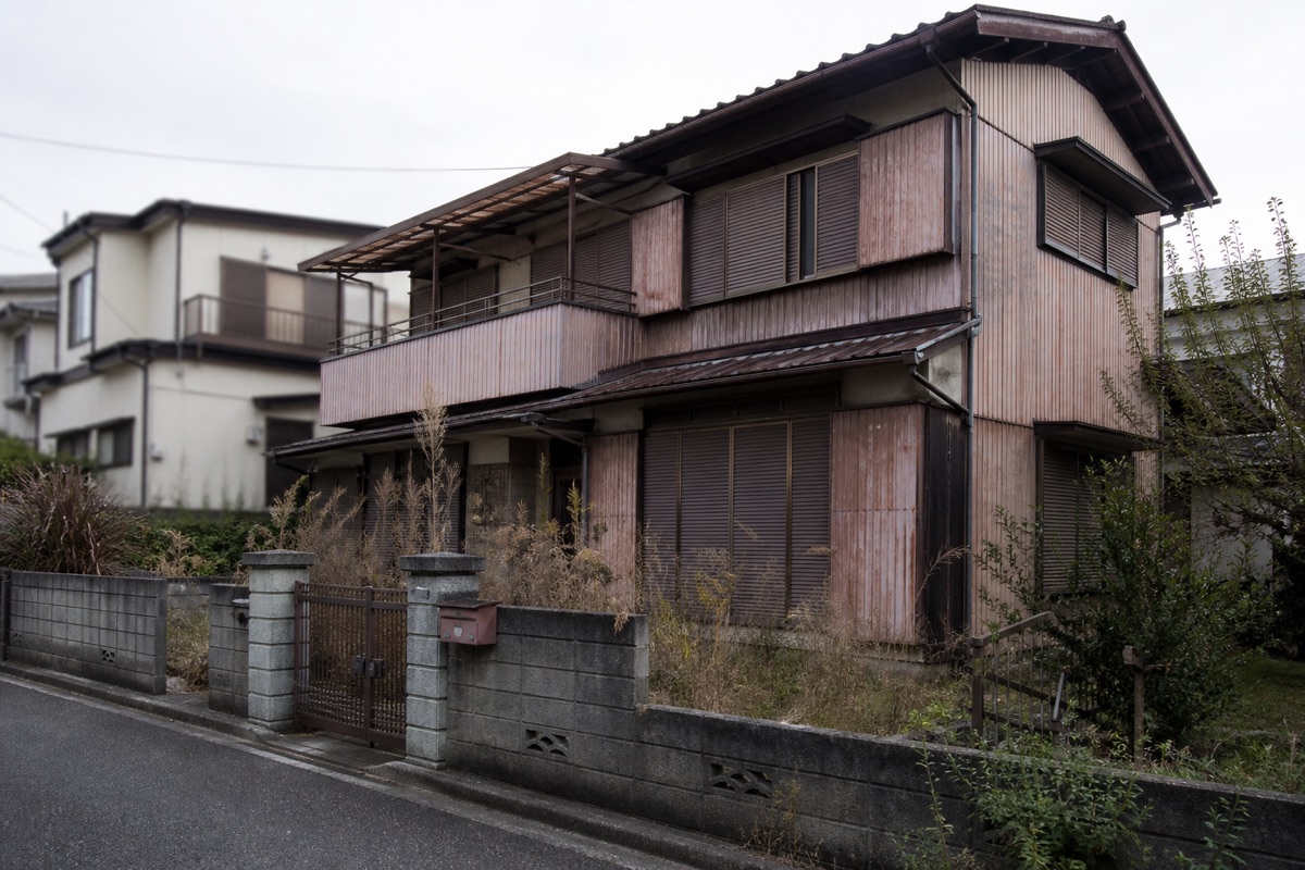 雨戸を閉め切り庭が草に覆われた郊外の古い木造空き家。疎遠な親族から相続することになる物件の例